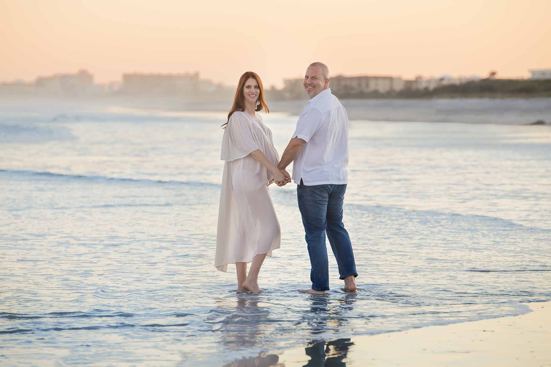 Pregnant woman holding hands with husband standing in the ocean