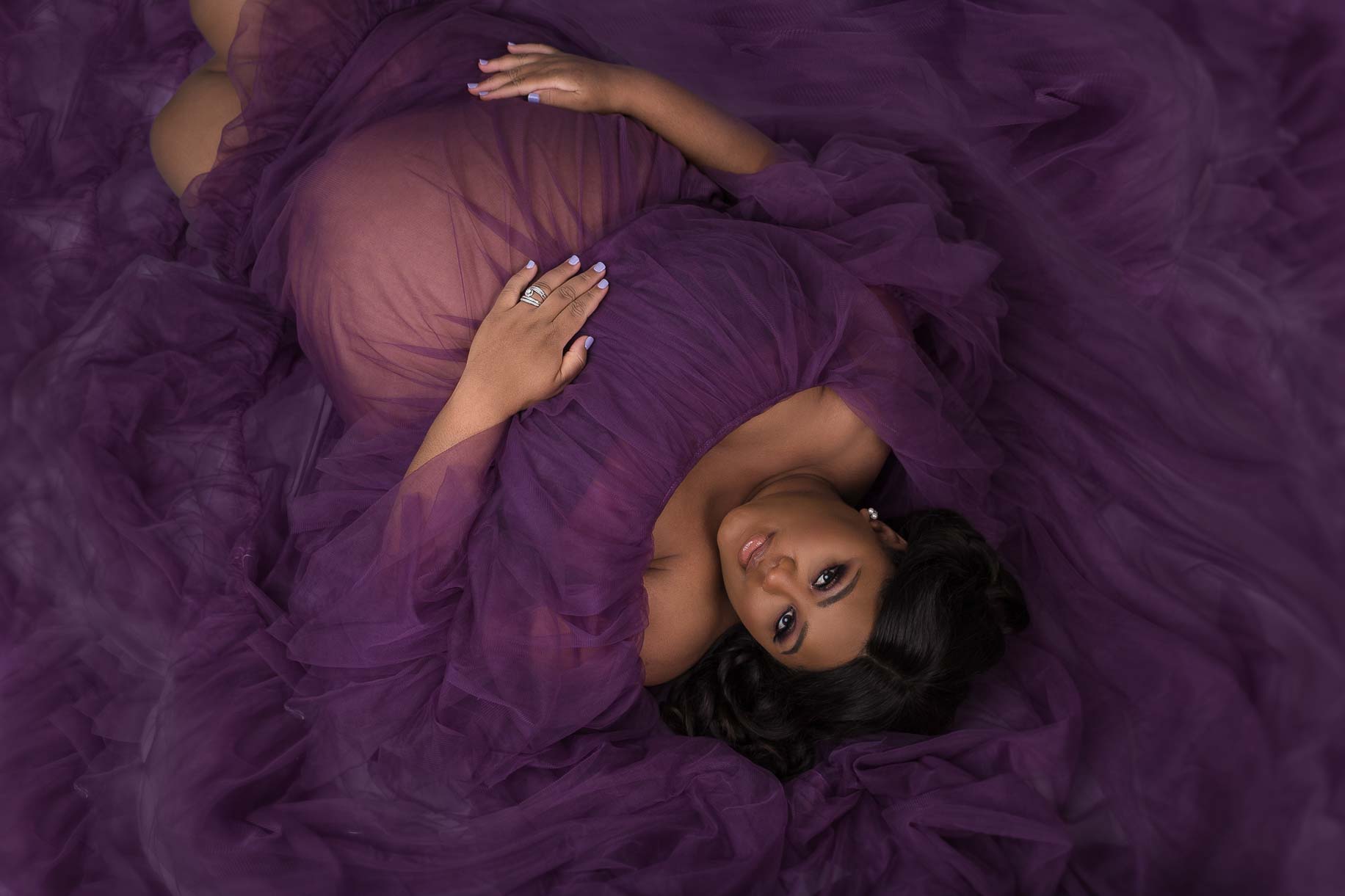 Pregnant woman lying on floor surrounded by purple tulle dress