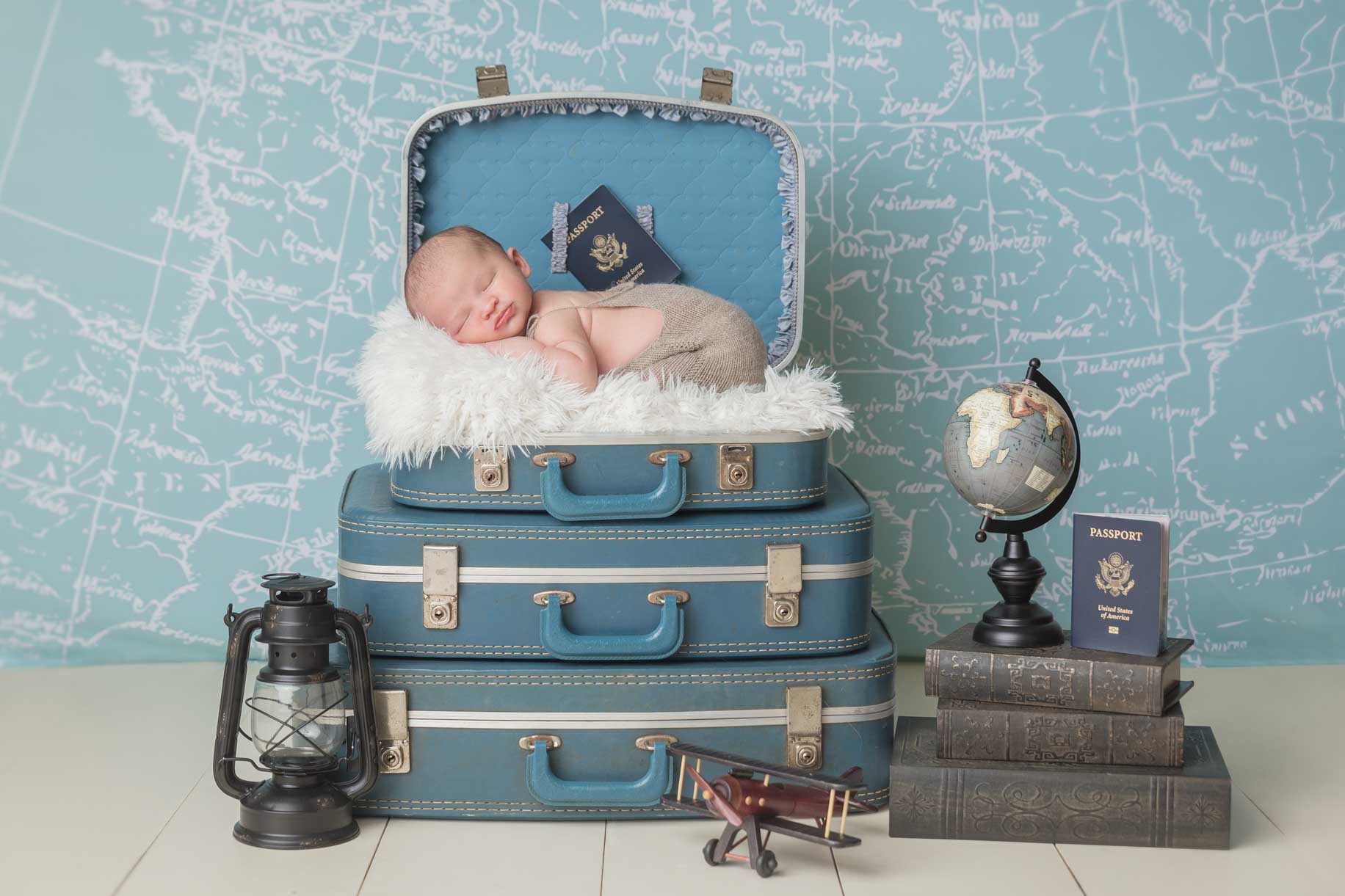 Newborn baby in suitcase surrounded by travel props