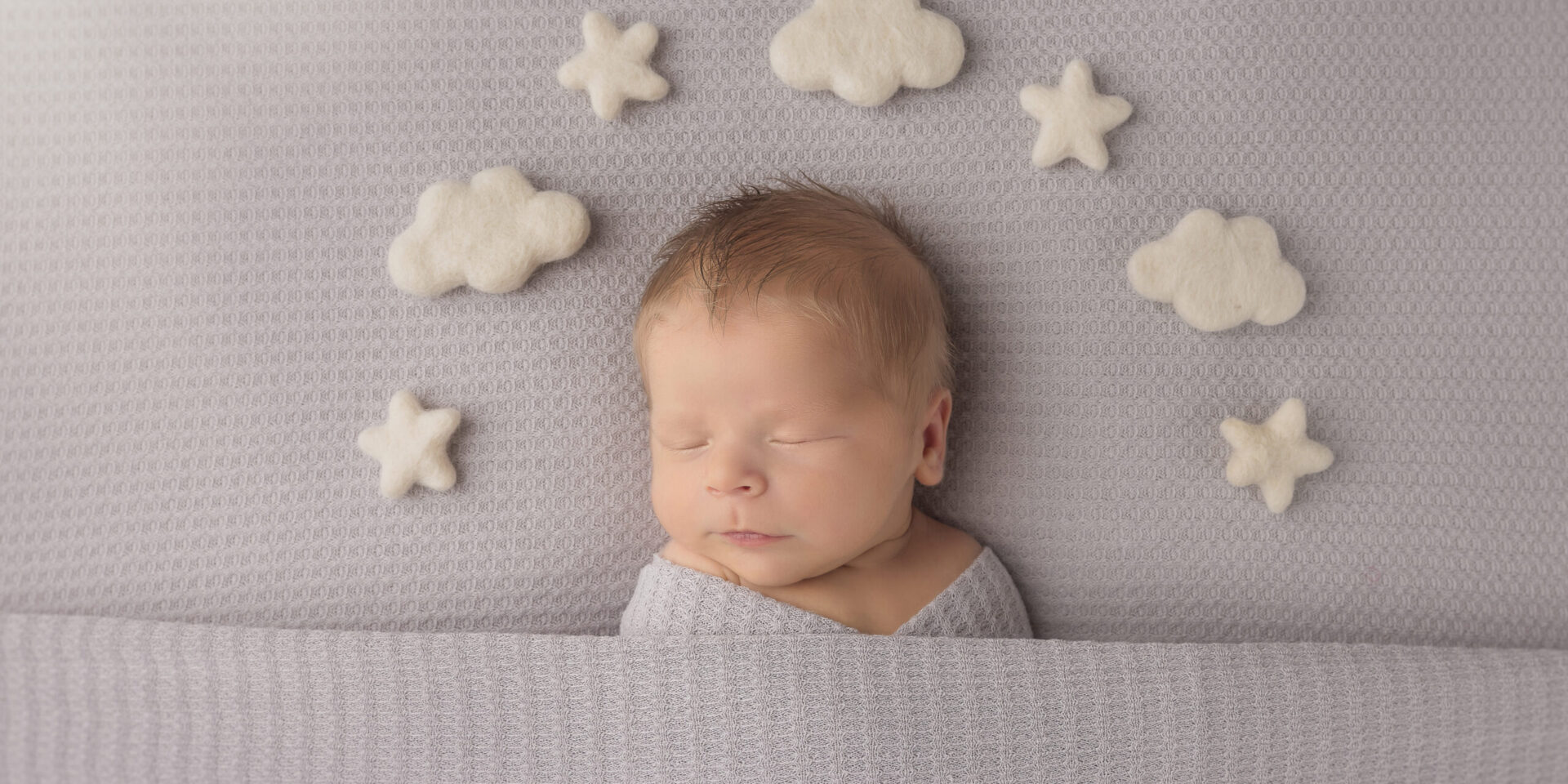 Newborn sleeping baby on gray background with clouds and stars around his head