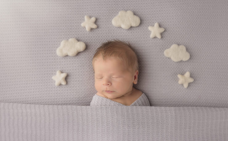Newborn sleeping baby on gray background with clouds and stars around his head