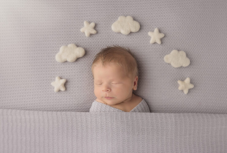 Newborn sleeping baby on gray background with clouds and stars around his head