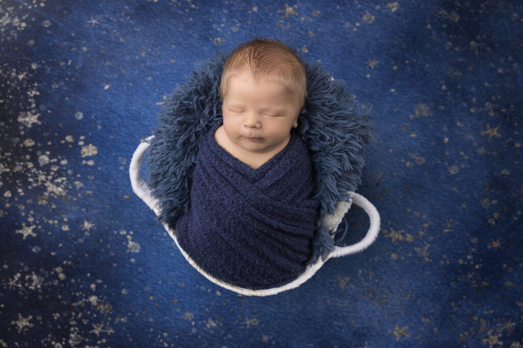 Sleeping newborn baby swaddled in blue blanket in a white basket on a blue background