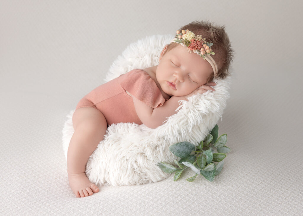 Newborn girl sleeping on furry white pillow with floral headband