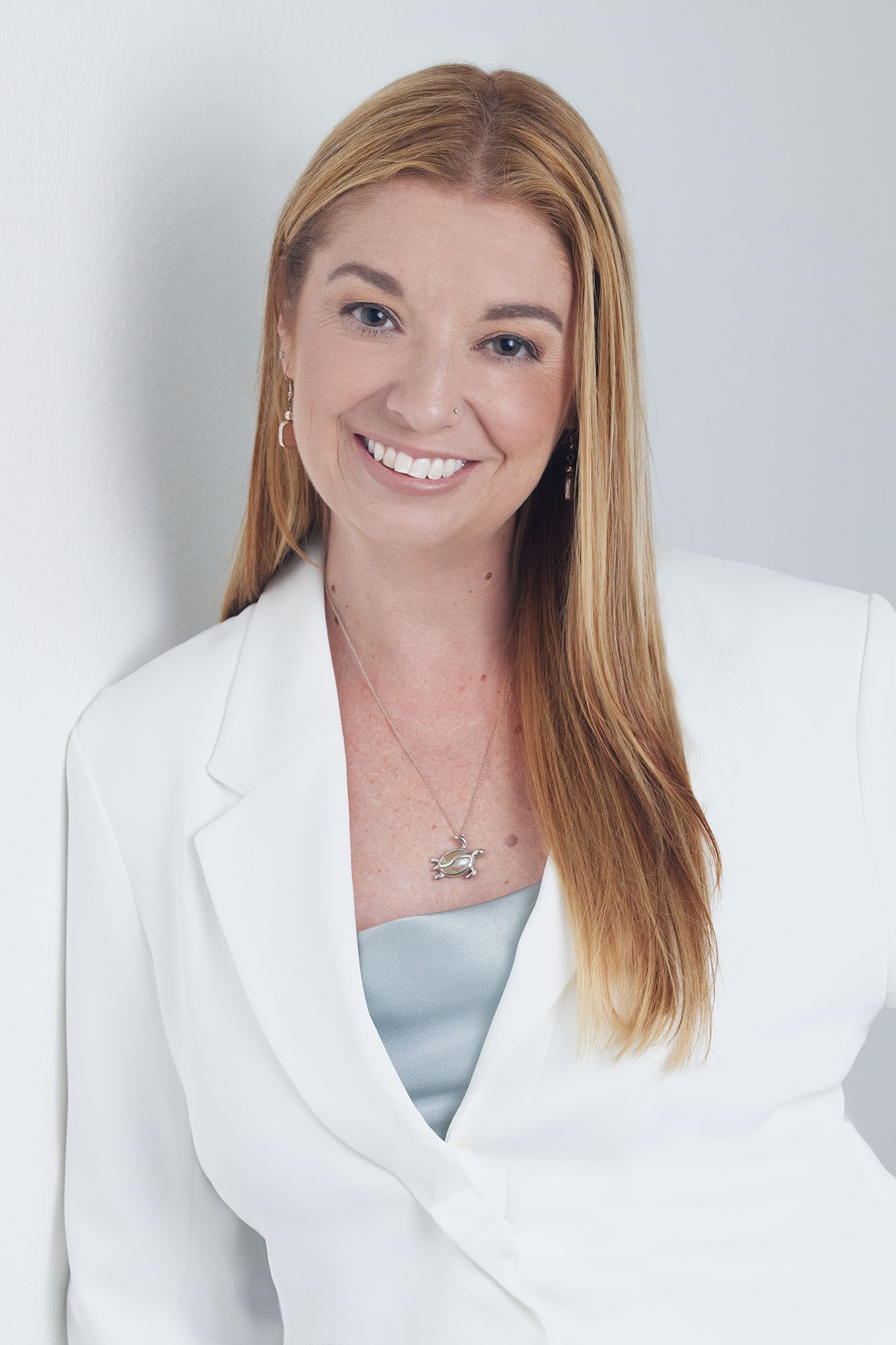 A woman leaning against a white wall for her headshot.