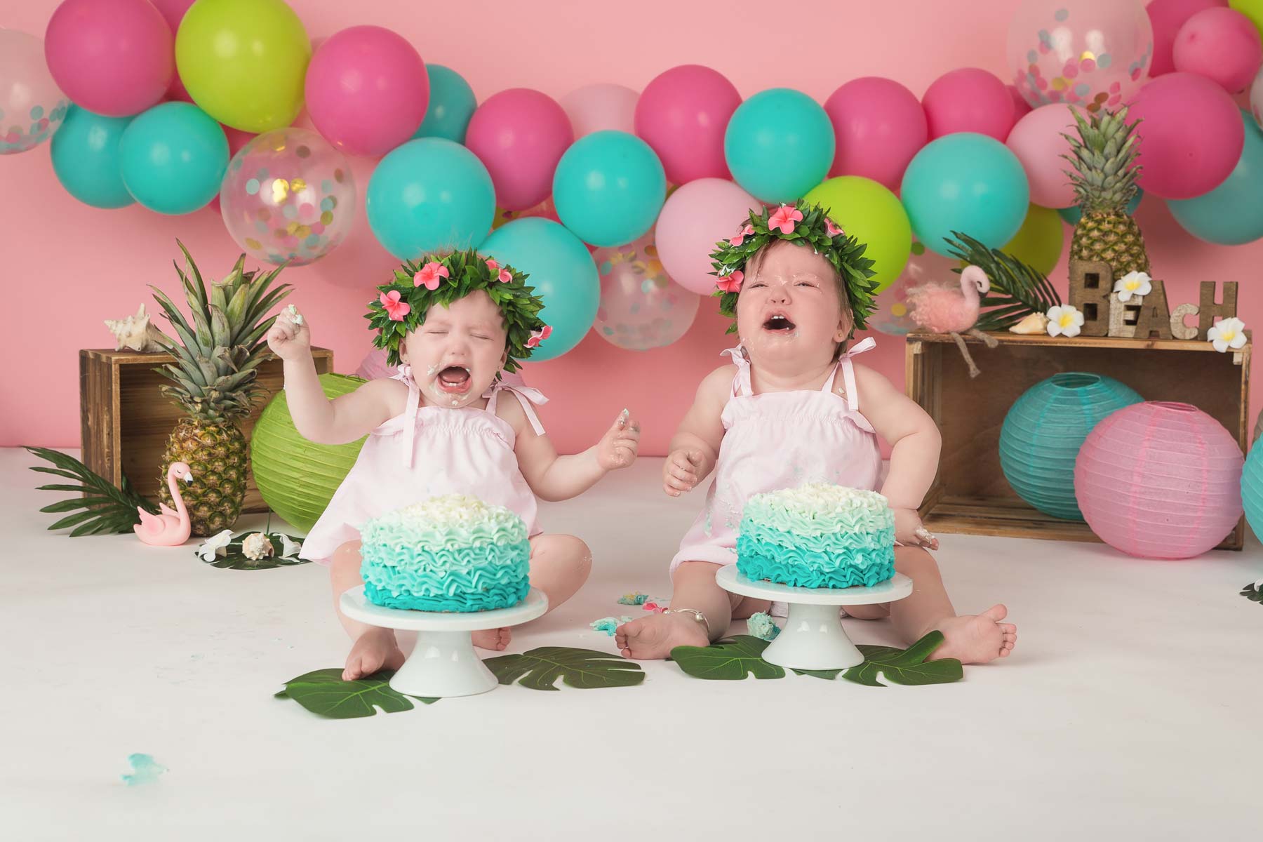 Crying twin girls are having their pictures taken during a tropical themed cake smash shoot.