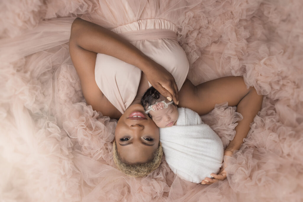 Mother laying upside down on pink fluffy blanket with sleeping newborn in write swaddle