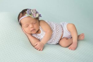 Posed newborn picture of a little girl sleeping on a aqua color blanket.