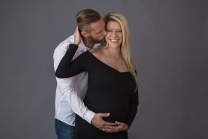 In-studio maternity picture of a father hugging and kissing the pregnant mother.