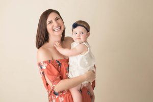 A dark haired Woman is smiling at the camera while holding her toddler.