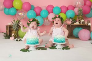 Twin girls are both crying sitting behind their cakes during a tropical themed cake smash session.