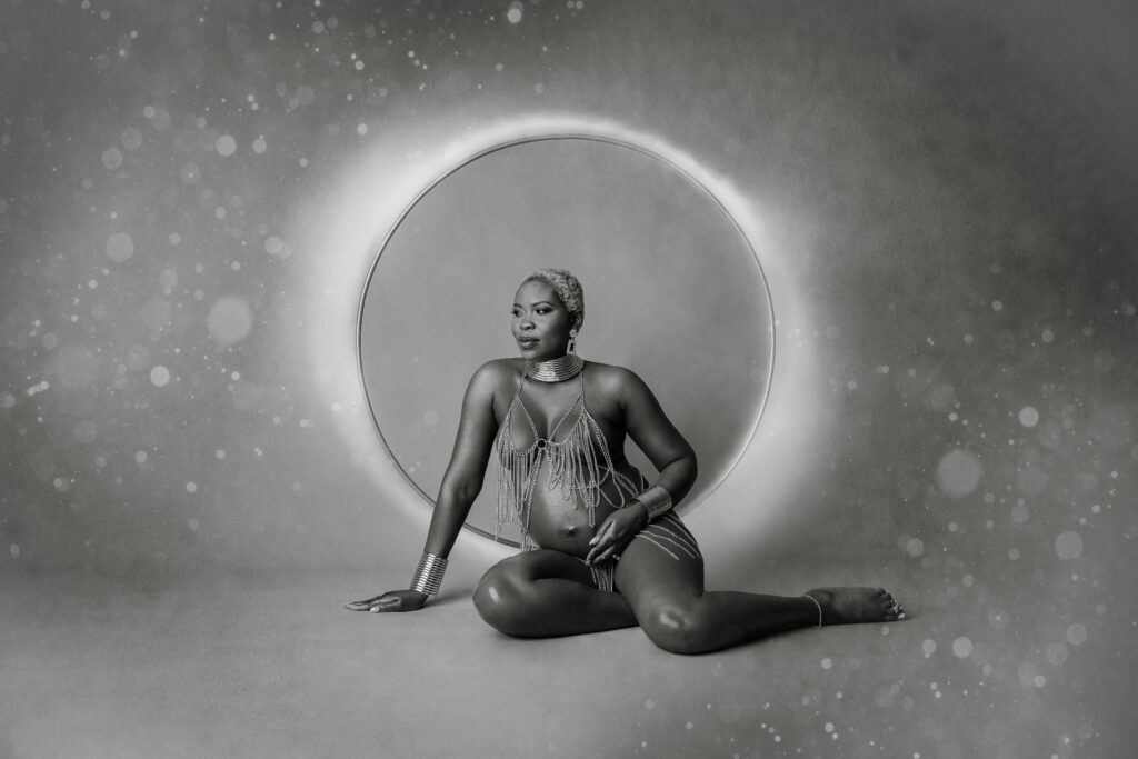 Pregnant woman sitting in front of moon backdrop looking to the side while holding belly