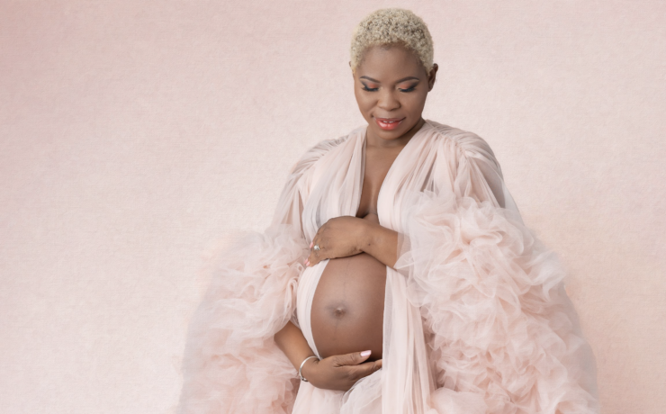 Pregnant woman on pink backdrop in pink robe, holding belly and looking down