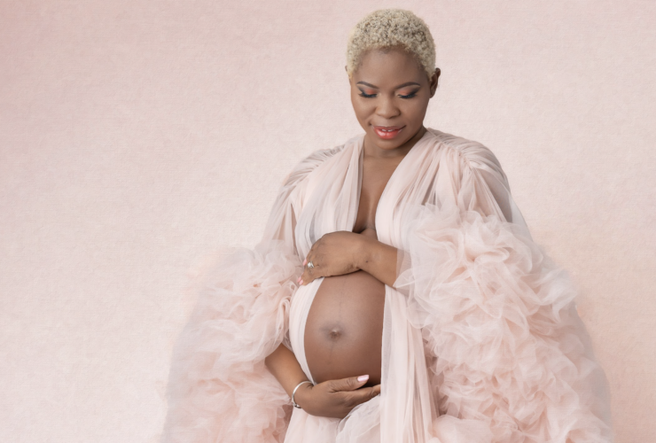 Pregnant woman on pink backdrop in pink robe, holding belly and looking down