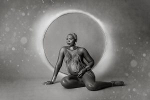 Contemporary black & white picture of a woman dressed only in a decorative chain necklace, sitting on the floor with circle effects in the background.